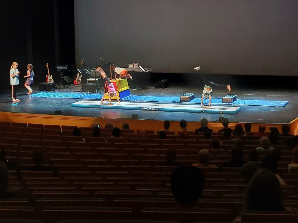 Lapsia tekemässä kärrynpyöriä ison salin lavalla.