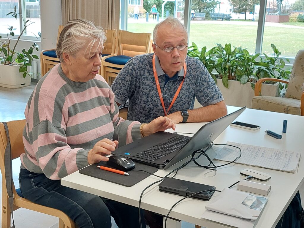 Nainen ja mies istuvat vierekkäin pöydän ääressä. Naisella on edessään kannettava tietokone.