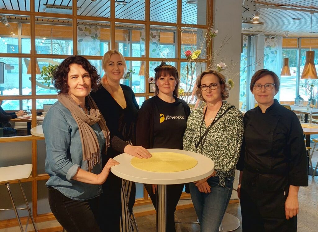 Viisi naista seisomassa pöydän ääressä.